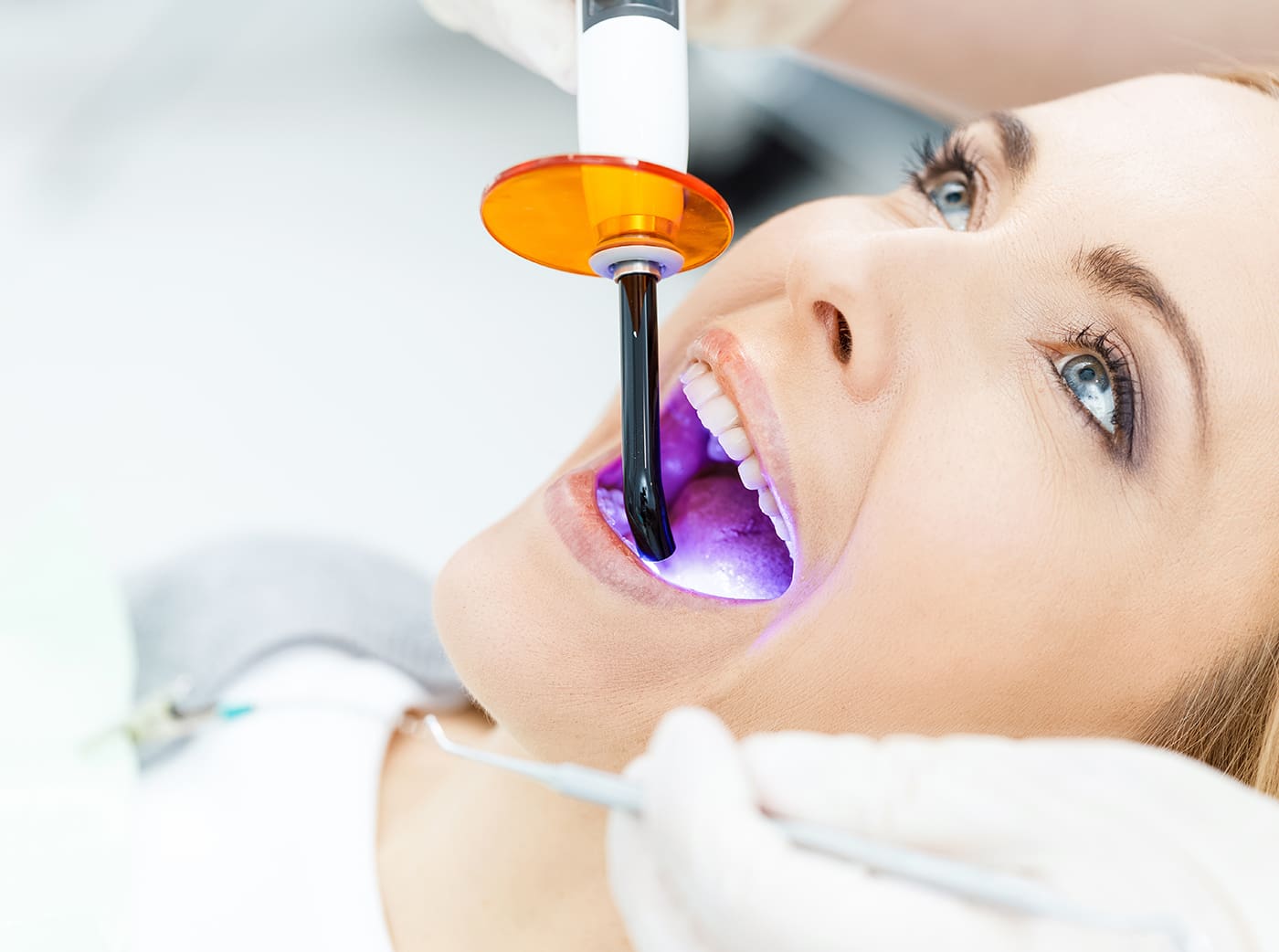Close-up partial view of dentist using dental curing UV lamp on teeth of patient